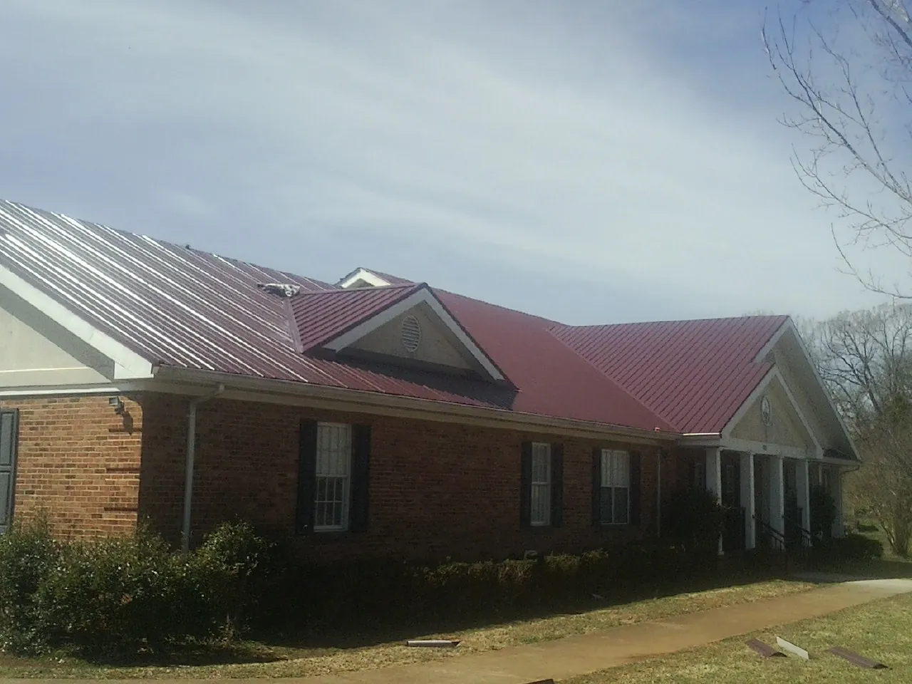 Red metal roof with gabled entries on a long brick building, from a Hail Damage Roof Repair job in Roca