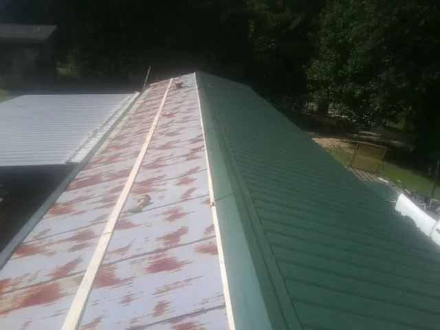 Old rusted panels beside newly installed green metal roofing — Wind Damage Roof Repair by Roofing Brothers in Roca