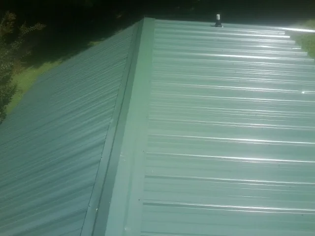 New green metal panels meeting at the ridge of a roof — Flat Roof Repair work by our crew in Roca