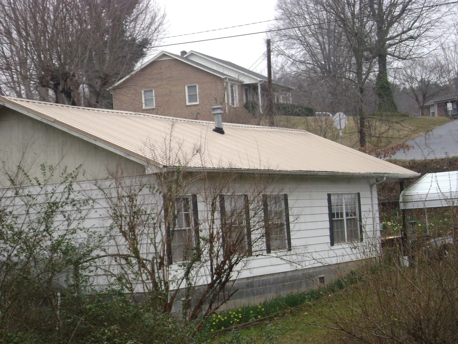 Tan metal roof on a white sided house set into a hillside — Commercial Roofing by Roofing Brothers in Roca