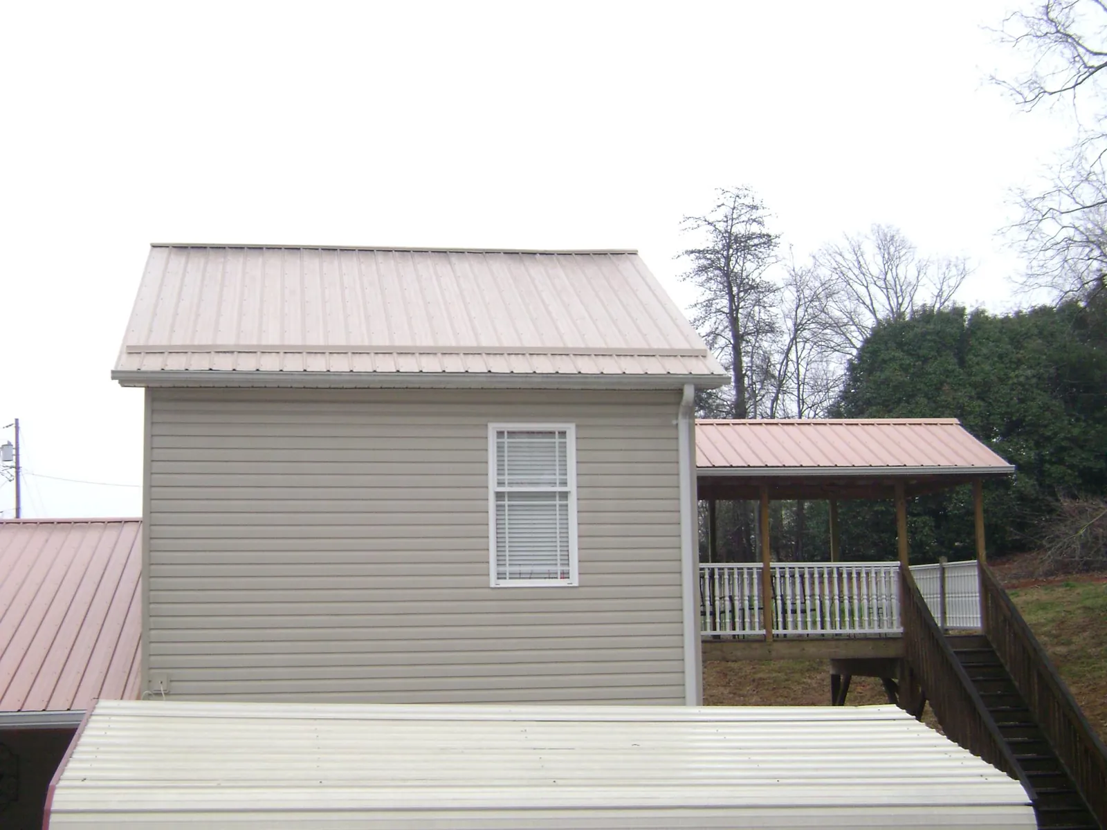 Tan metal roofs on a two story addition and attached porch, from a Roof Replacement job in Roca